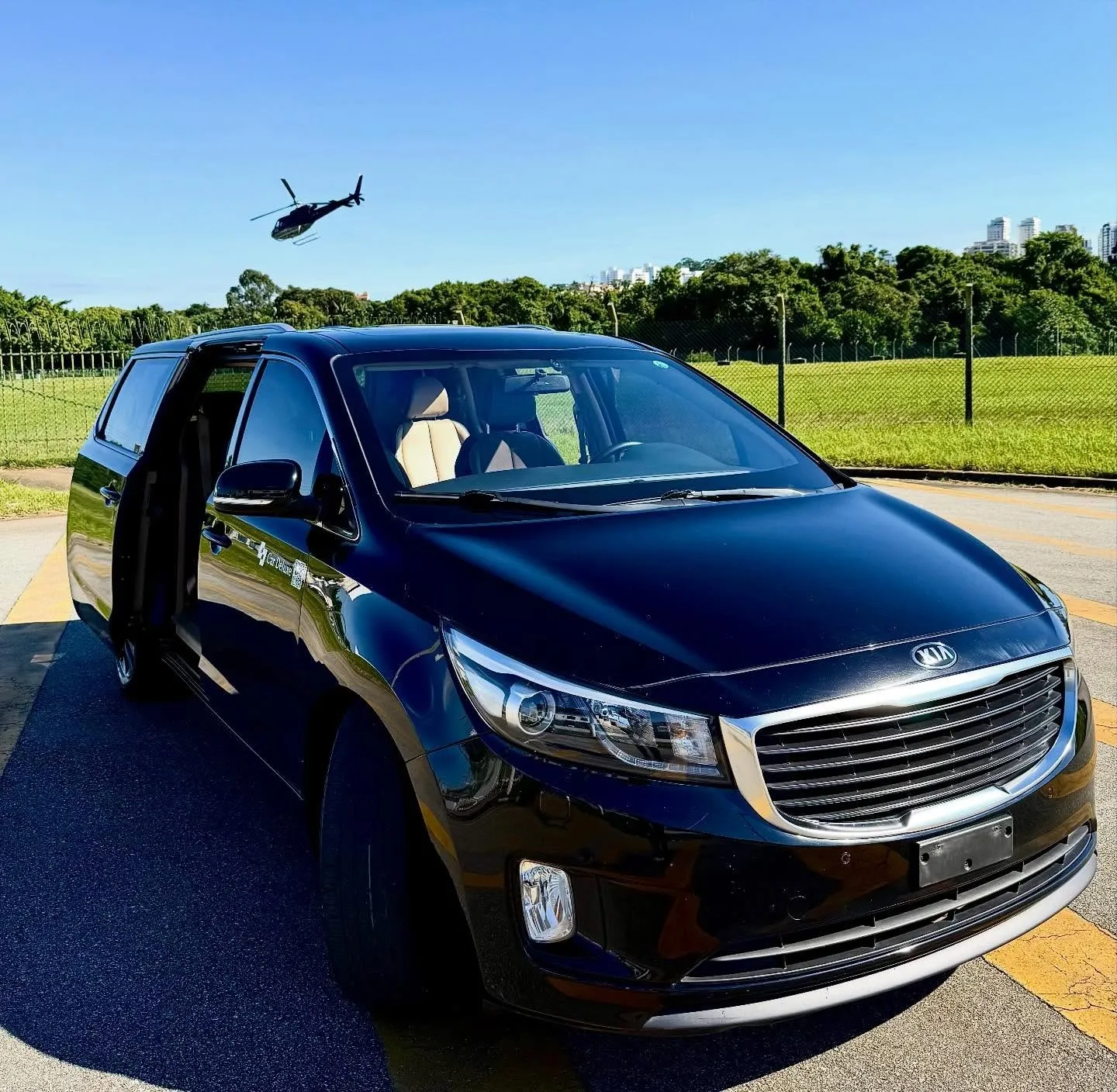 Kia Grand Carnival no Campo de Marte com um helicóptero ao fundo